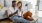 a man and woman with take out, sit against a couch on their living room floor and watch at their cell phone